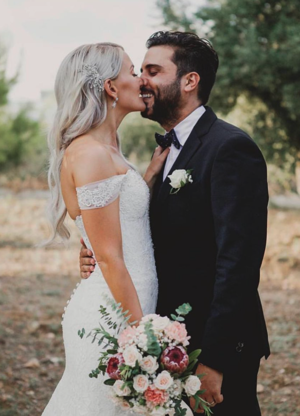 Novios besándose al aire libre con ramo nupcial