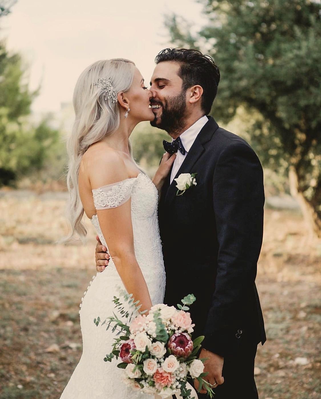 Bride and groom sharing a kiss outdoors with bridal bouquet